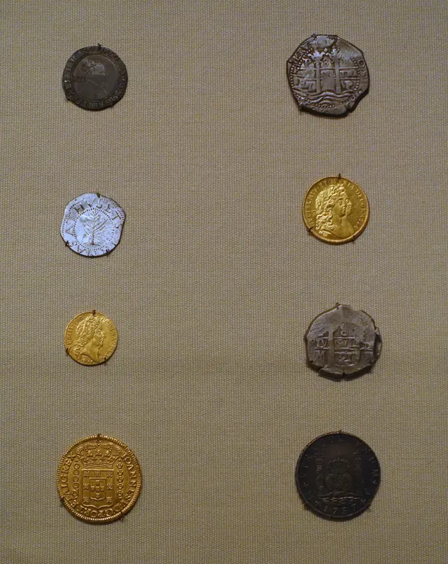 Museum display of coins used in colonial America: Spanish and Bolivian pieces of eight, English and French gold, and a Massachusetts Pine Tree shilling