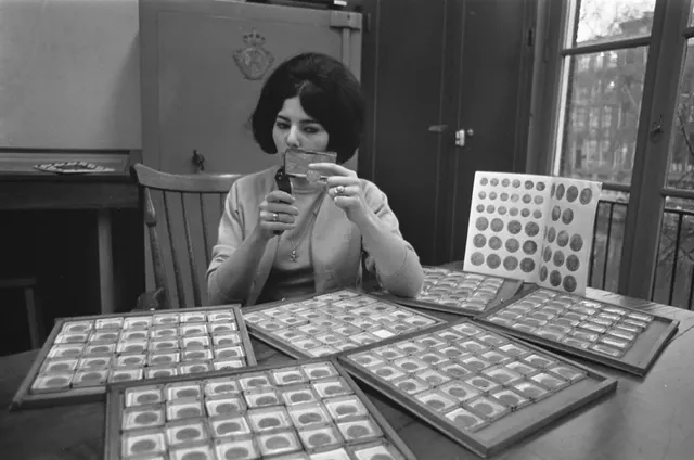A man at a 1966 coin auction viewing in Serooskerke, the Netherlands, inspecting gold coins through a loupe