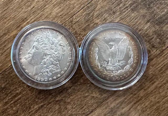 Two toned Morgan silver dollars in clear round capsules, one showing the obverse and one the reverse