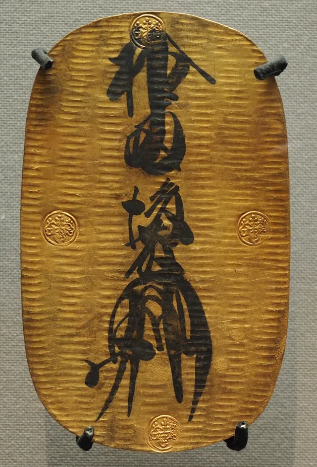 Keicho oban, a large oval gold plate about 15 cm long, with a brush-ink inscription reading ten ryo and the Goto signature between four stamped paulownia crests