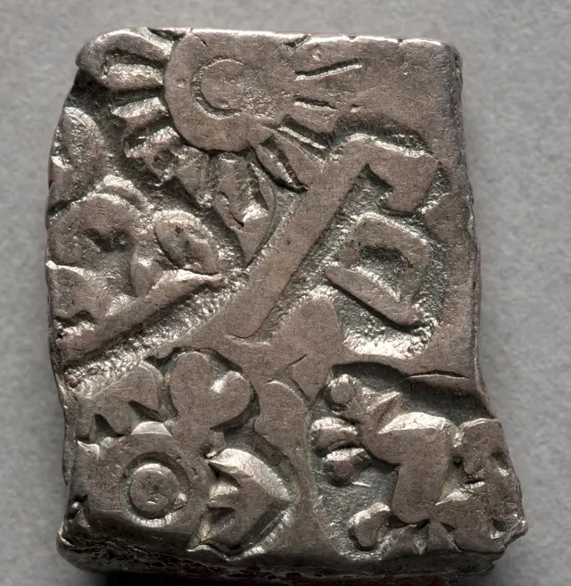 Close-up of a rectangular Mauryan silver punch-marked coin showing a sun, a six-armed symbol and other stamped marks