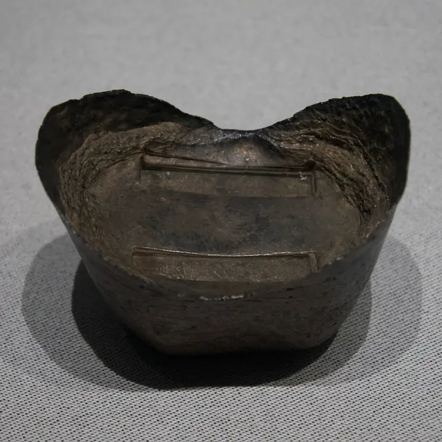 A boat-shaped 50-tael silver sycee from 1877, cast for Anhui salt-tax payments, with raised ends and stamped inscriptions in the centre